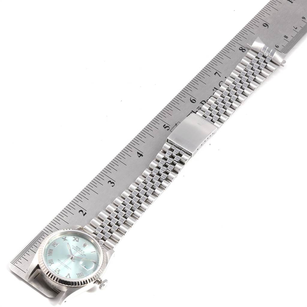 The image shows a top-down view of a Rolex Datejust 16234 Men's Stainless Steel Blue Dial 16234 Men's Stainless Steel Blue Dial watch, featuring its silver dial, bezel, and steel bracelet next to a ruler.