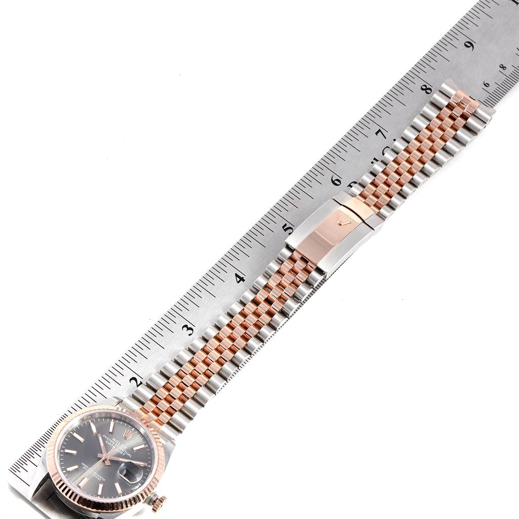 This image shows a Rolex Datejust 126231 Men
s Steel and Gold (two tone) Grey Dial 126231 Men
s Steel and Gold (two tone) Grey Dial watch laid flat beside a ruler, highlighting its bracelet and clasp.