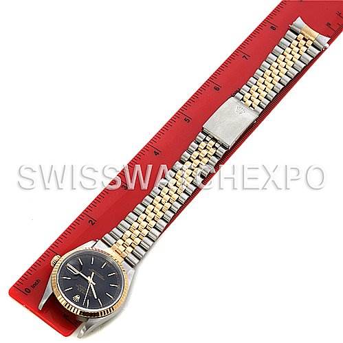 The Rolex Datejust 16233 Men's Stainless Steel Black Dial 16233 Men's Stainless Steel Black Dial watch is shown from a top-down angle, highlighting its black dial, fluted bezel, and Jubilee bracelet alongside a red measuring ruler.