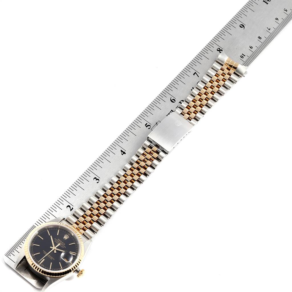 The Rolex Datejust 16233 Men
s Steel and Gold (two tone) Black Dial 16233 Men
s Steel and Gold (two tone) Black Dial watch is shown from a top-down angle, featuring its dial, bezel, bracelet, and clasp next to a ruler.