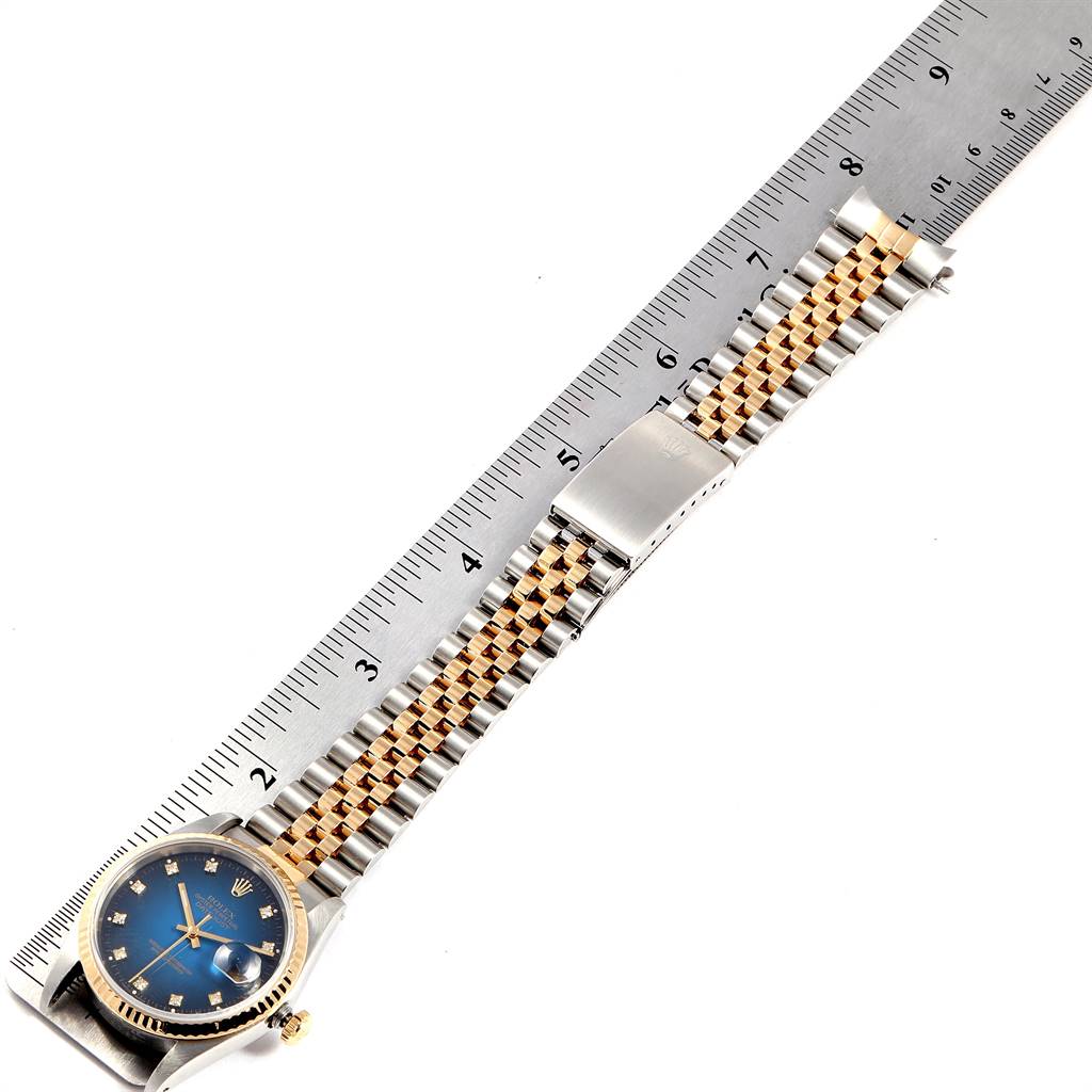 The image shows a Rolex Datejust 16233 Men
s Steel and Gold (two tone) Blue Dial 16233 Men
s Steel and Gold (two tone) Blue Dial watch positioned alongside a ruler, displaying its face and bracelet.