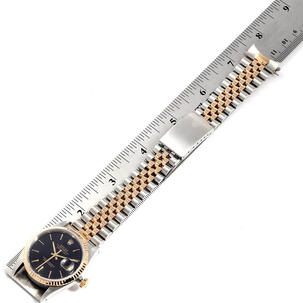 The image shows a Rolex Datejust 16233 Men's Steel and Gold (two tone) Black Dial 16233 Men's Steel and Gold (two tone) Black Dial watch laid flat next to a ruler, highlighting the watch's face and bracelet.