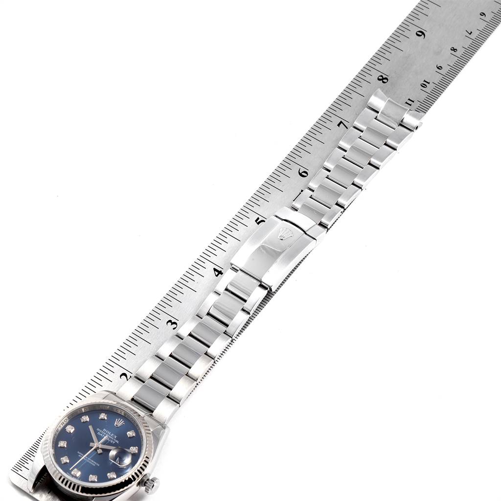 The image shows a Rolex Datejust 116234 Men's Stainless Steel Blue Dial 116234 Men's Stainless Steel Blue Dial watch laid flat alongside a ruler, displaying its band, clasp, and partial face.