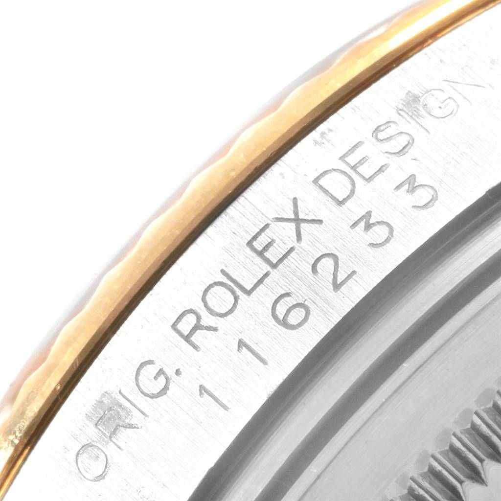 This close-up image shows the side of the Rolex Datejust 116233 Men's Steel and Gold (two tone) Silver Dial 116233 Men's Steel and Gold (two tone) Silver Dial bezel with engraved text and part of the fluted edge.