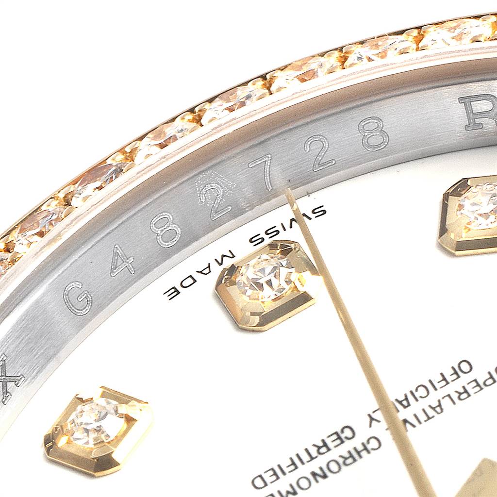 The image shows a close-up of the Rolex Datejust 116243 Men's Steel and Gold (two tone) White Dial 116243 Men's Steel and Gold (two tone) White Dial's bezel with embedded diamonds, part of the dial, and an engraved serial number.