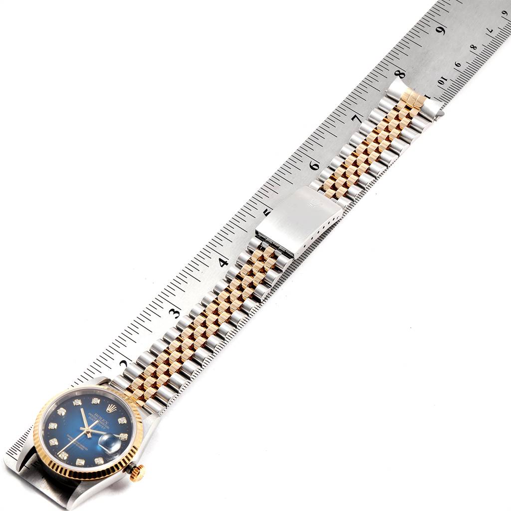 The image shows a Rolex Datejust 16233 Men's Steel and Gold (two tone) Blue Dial 16233 Men's Steel and Gold (two tone) Blue Dial watch lying flat next to a ruler, displaying its blue dial and Jubilee bracelet.