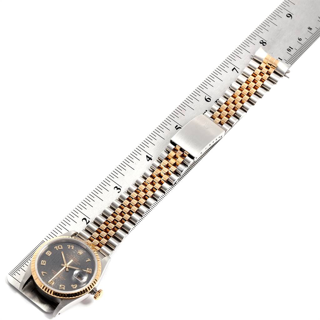 The Rolex Datejust 16233 Men's Steel and Gold (two tone) Grey Dial 16233 Men's Steel and Gold (two tone) Grey Dial watch is shown from an overhead angle, featuring its face, bracelet, and clasp placed on a ruler.