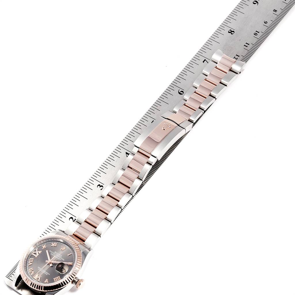 The Rolex Datejust 126231 Men's Steel and Gold (two tone) Grey Dial 126231 Men's Steel and Gold (two tone) Grey Dial watch is shown from an aerial view, highlighting its bracelet and clasp alongside a ruler for scale.