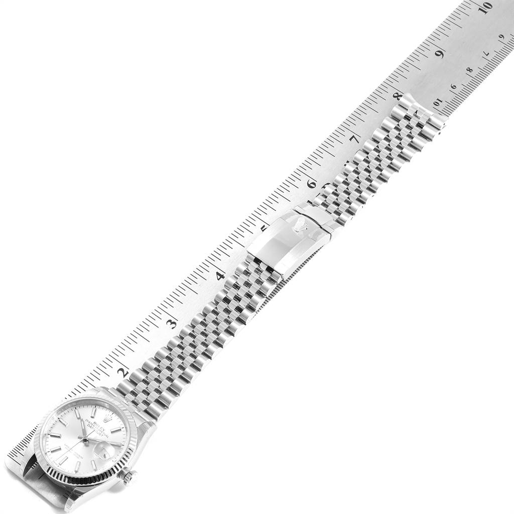 The image shows a silver Rolex Datejust 126234 Men's Stainless Steel Silver Dial 126234 Men's Stainless Steel Silver Dial watch with a Jubilee bracelet, laid parallel next to a ruler.