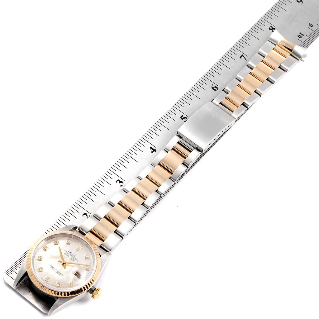 The Rolex Datejust 16233 Men's Steel and Gold (two tone) Mother of Pearl Dial 16233 Men's Steel and Gold (two tone) Mother of Pearl Dial watch is shown at an overhead angle, displaying its band, clasp, and face beside a ruler.