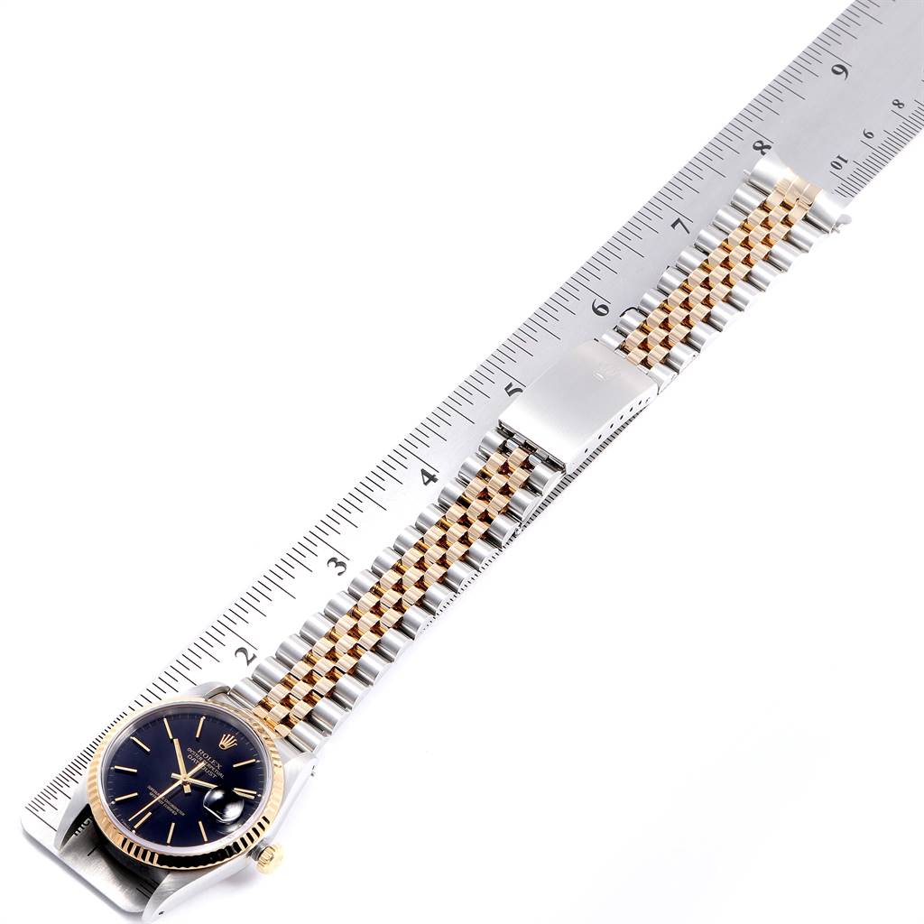 The image shows a Rolex Datejust 16233 Men
s Steel and Gold (two tone) Black Dial 16233 Men
s Steel and Gold (two tone) Black Dial watch angled diagonally, featuring its face, gold bezel, and two-tone metal bracelet measured against a ruler.