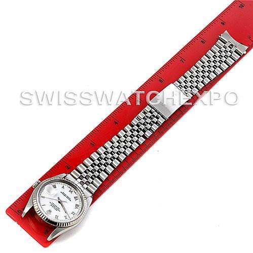 This image shows a top-down view of a Rolex Datejust 16234 Men's Stainless Steel White Dial 16234 Men's Stainless Steel White Dial watch with a silver bracelet laid against a red ruler.