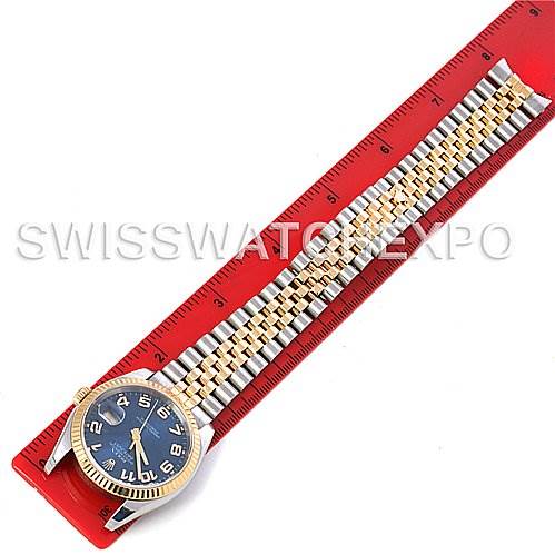 The Rolex Datejust 116233 Men
s Stainless Steel Blue Dial 116233 Men
s Stainless Steel Blue Dial watch is shown from top-down, displaying the dial, bezel, and bracelet, placed on a red ruler.