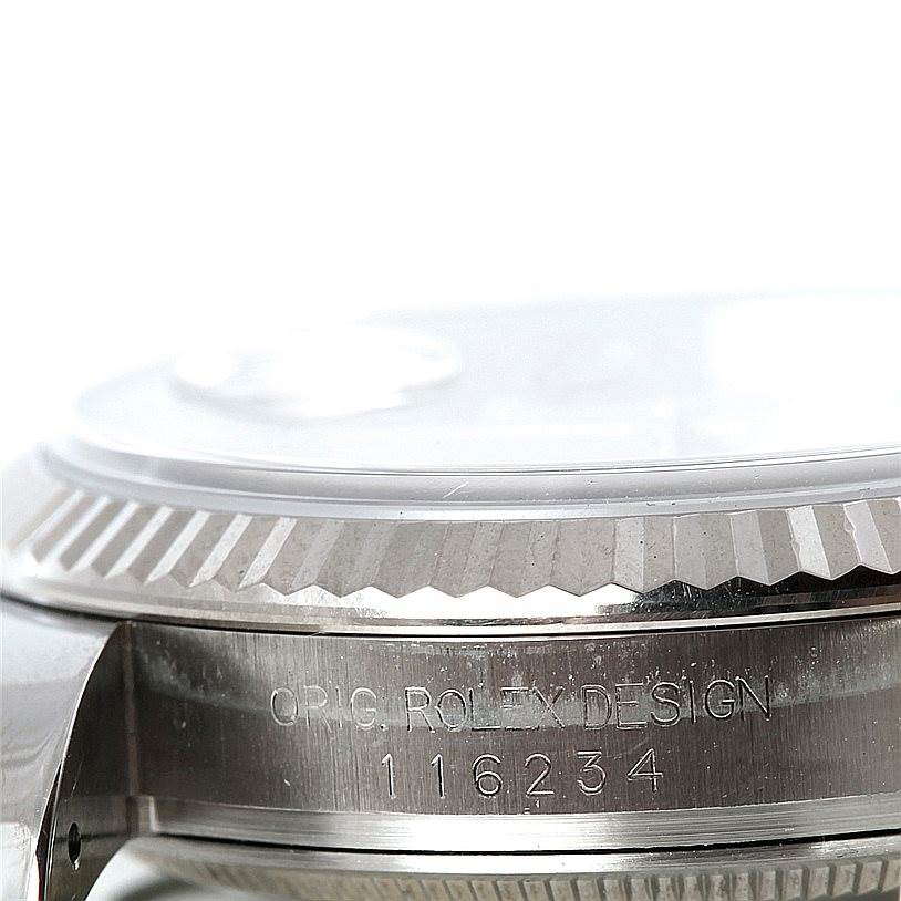 The image shows a close-up of the side of a Rolex Datejust 116234 Men's Stainless Steel Silver Dial 116234 Men's Stainless Steel Silver Dial watch, detailing its engraved serial number and fluted bezel.