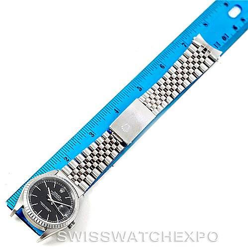 This Rolex Datejust 16220 Men
s Stainless Steel Black Dial 16220 Men
s Stainless Steel Black Dial watch is shown laid flat beside a blue ruler, highlighting its face, bracelet, and clasp.