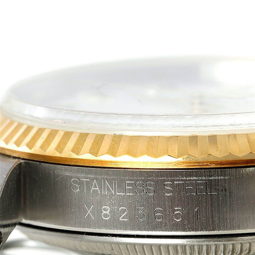 This close-up of a Rolex Datejust 16233 Men's Steel and Gold (two tone) White Dial 16233 Men's Steel and Gold (two tone) White Dial watch showcases part of the bezel, crystal, and stainless steel case with engravings.