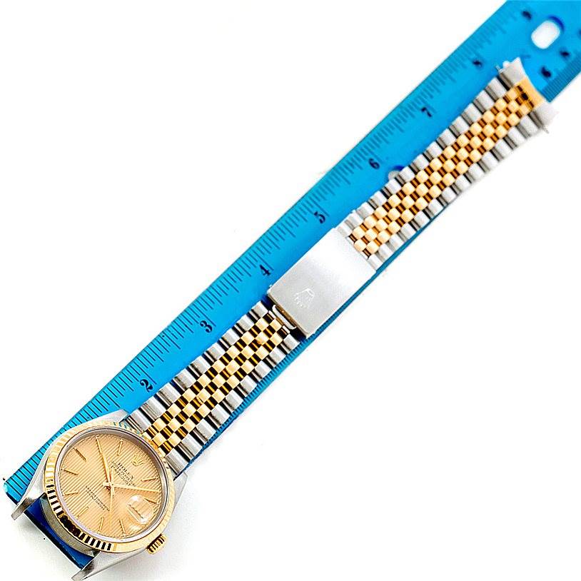 This image shows a Rolex Datejust 16233 Men's Steel and Gold (two tone) Champagne Dial 16233 Men's Steel and Gold (two tone) Champagne Dial watch face-up alongside a blue ruler, highlighting the watch's dial, bezel, and bracelet.