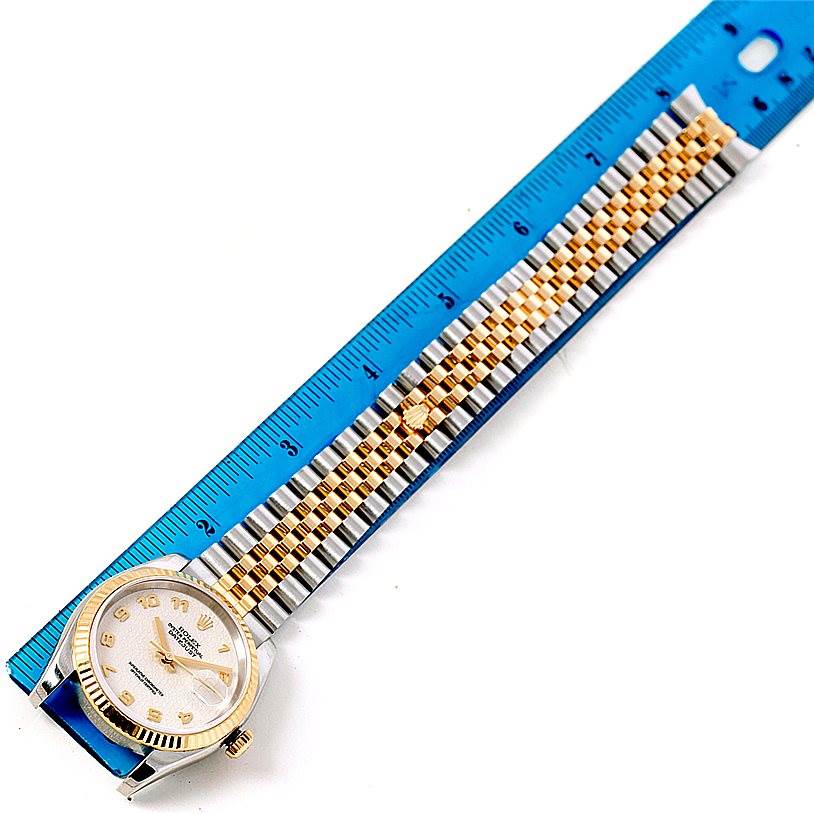 A Rolex Datejust 116233 Men's Stainless Steel Beige Dial 116233 Men's Stainless Steel Beige Dial watch is displayed with a metal band and a blue ruler for scale, viewed from above.