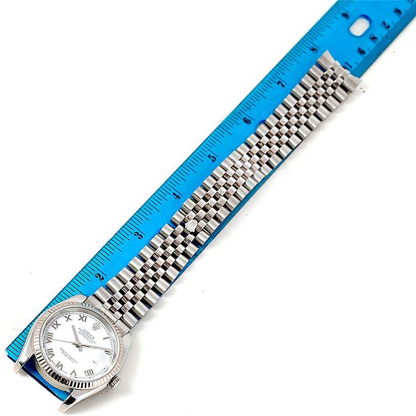 The image shows a Rolex Datejust 116234 Men
s Stainless Steel White Dial 116234 Men
s Stainless Steel White Dial watch laid flat alongside a blue ruler, displaying its face and jubilee bracelet.