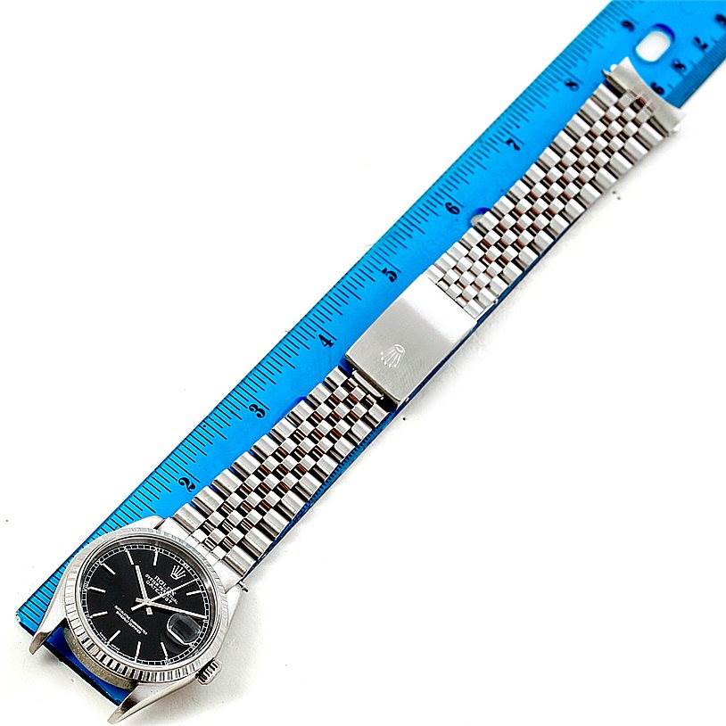 The image shows a top-down view of a Rolex Datejust 16220 Men
s Stainless Steel Black Dial 16220 Men
s Stainless Steel Black Dial watch with its band extended next to a blue ruler.