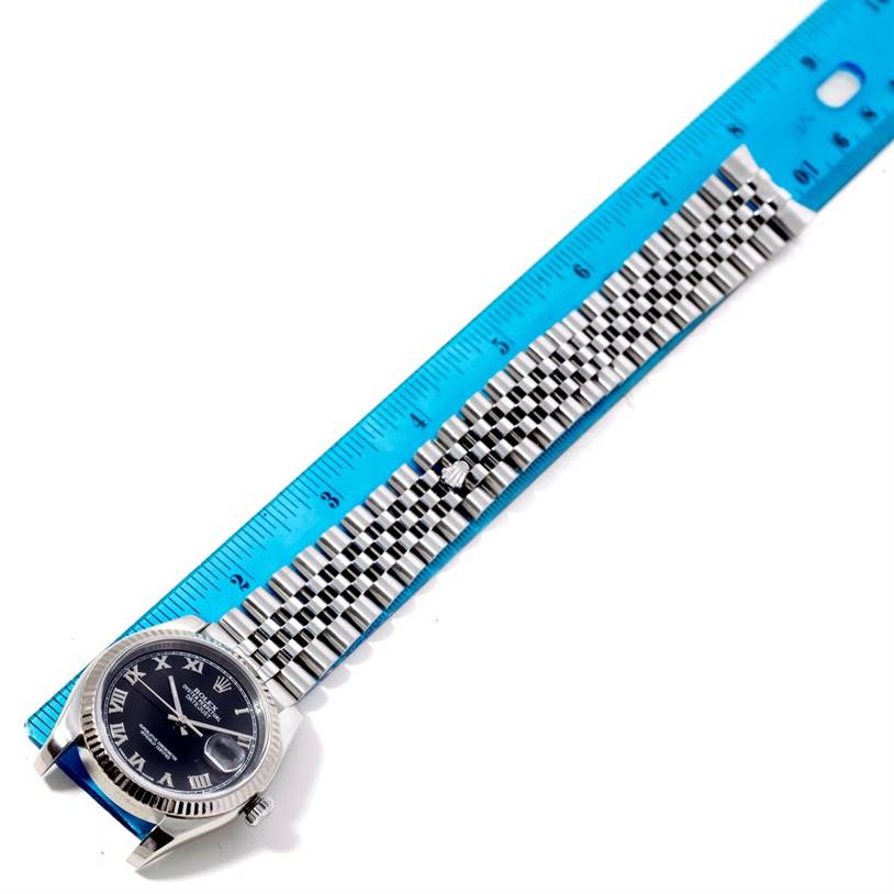 The image shows a Rolex Datejust 116234 Men
s Stainless Steel Black Dial 116234 Men
s Stainless Steel Black Dial watch laid flat with a blue ruler measuring the length of its bracelet.