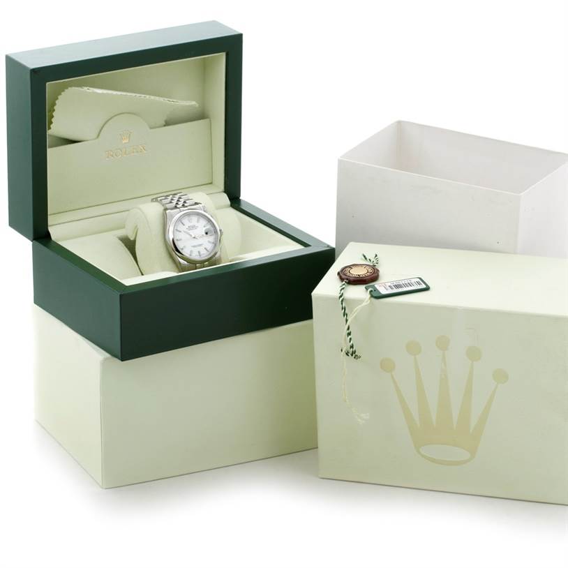 The image shows a Rolex Datejust 116200 Men
s Stainless Steel White Dial 116200 Men
s Stainless Steel White Dial watch from a front angle, displayed in its box with additional packaging and accessories beside it.