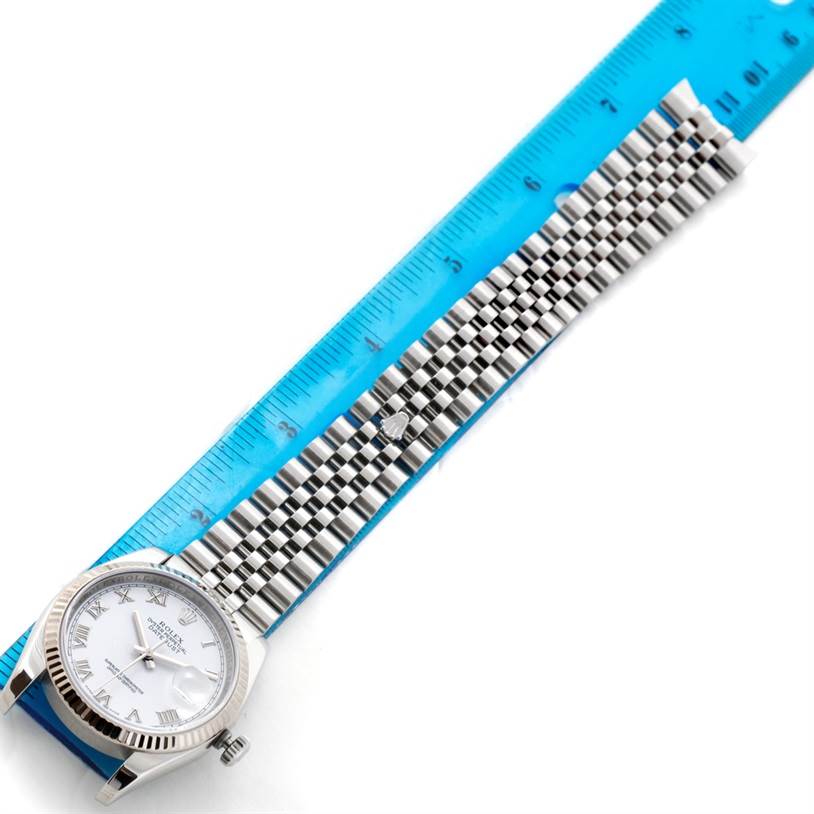 The Rolex Datejust 116234 Men
s Stainless Steel White Dial 116234 Men
s Stainless Steel White Dial watch is shown from a top-down angle, displaying the face, bezel, and metal bracelet next to a blue ruler.