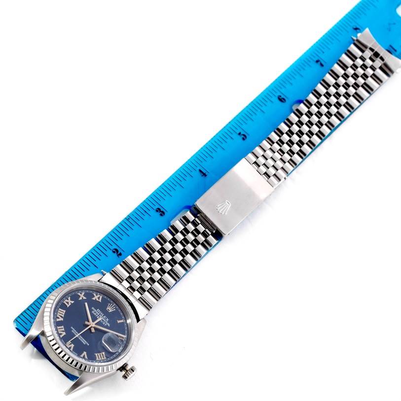 The Rolex Datejust 16220 Men's Stainless Steel Blue Dial 16220 Men's Stainless Steel Blue Dial watch is shown laid flat with its dial, bezel, crown, and metal bracelet visible next to a blue ruler.