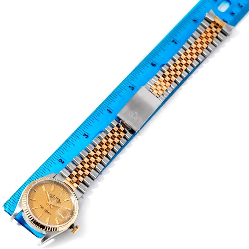 The Rolex Datejust 16233 Men's Steel and Gold (two tone) Champagne Dial 16233 Men's Steel and Gold (two tone) Champagne Dial watch is shown from a top-down angle, displaying the face, crown, and full bracelet length against a blue ruler.
