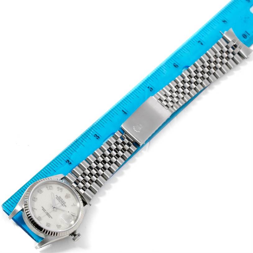 This image shows a top-down view of a Rolex Datejust 16234 Men's Stainless Steel Silver Dial 16234 Men's Stainless Steel Silver Dial watch with its stainless steel bracelet aligned next to a ruler.