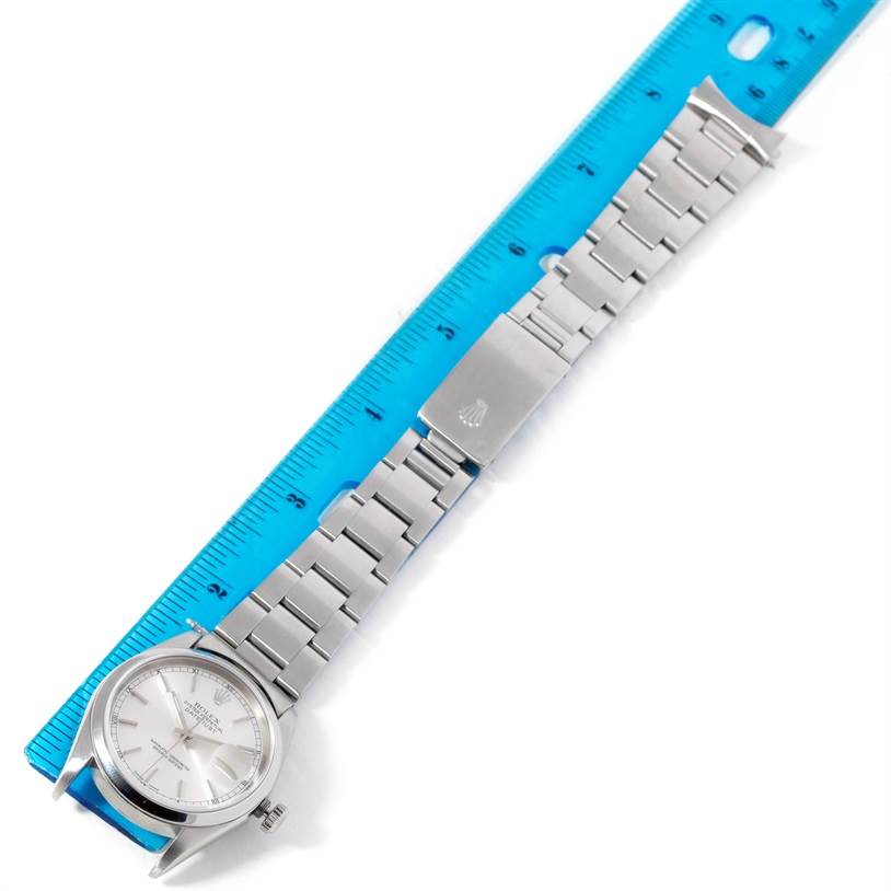 The Rolex Datejust 16200 Men's Stainless Steel Silver Dial 16200 Men's Stainless Steel Silver Dial watch is shown from an overhead angle with its metal bracelet stretched out alongside a blue ruler.