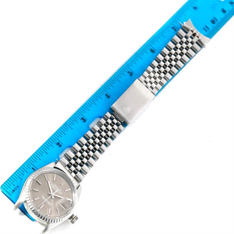 The image shows a Rolex Datejust 16030 Men
s Stainless Steel Grey Dial 16030 Men
s Stainless Steel Grey Dial watch laid flat next to a blue ruler, revealing the face, bezel, crown, and bracelet in detail.