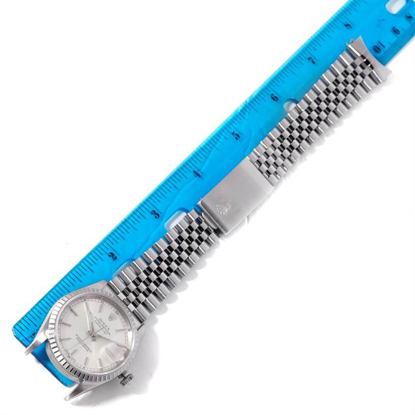 The image shows a top view of a Rolex Datejust 16220 Men's Stainless Steel Silver Dial 16220 Men's Stainless Steel Silver Dial watch with a Oystersteel bracelet beside a blue ruler for scale.