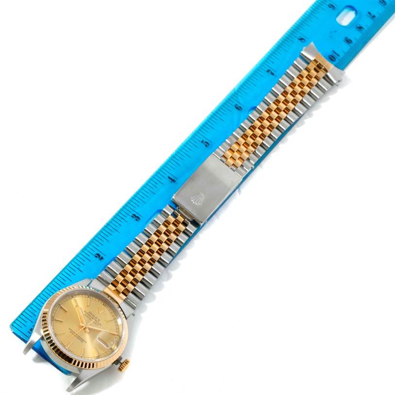 The Rolex Datejust 16233 Men's Steel and Gold (two tone) Champagne Dial 16233 Men's Steel and Gold (two tone) Champagne Dial watch is shown laid flat with its bracelet fully extended alongside a blue ruler for measurement.