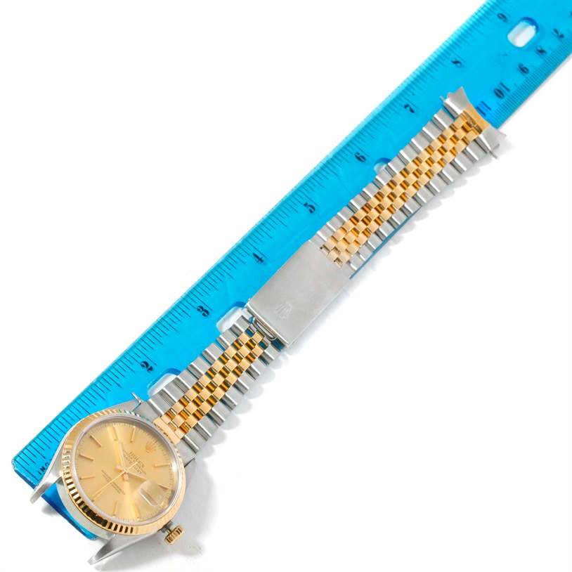 The image shows a Rolex Datejust 16233 Men's Steel and Gold (two tone) Champagne Dial 16233 Men's Steel and Gold (two tone) Champagne Dial watch laid flat next to a blue ruler, highlighting the face, bracelet, and clasp.