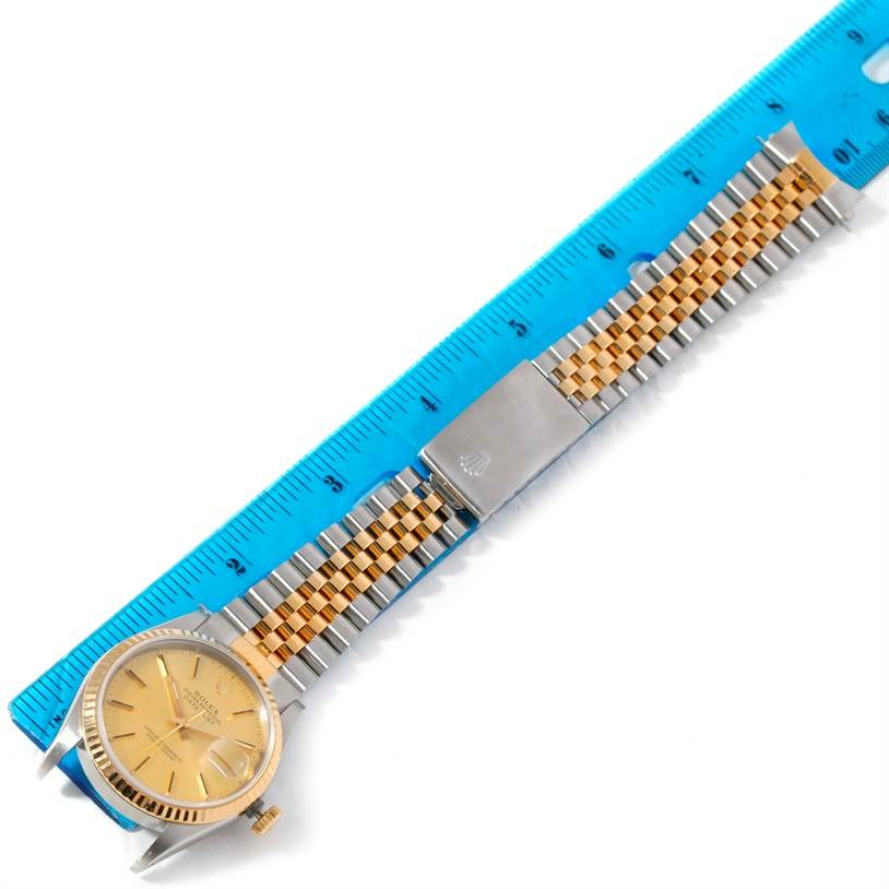 This image shows a Rolex Datejust 16233 Men's Steel and Gold (two tone) Champagne Dial 16233 Men's Steel and Gold (two tone) Champagne Dial watch laid flat beside a blue ruler, displaying its gold dial and two-tone metal bracelet.