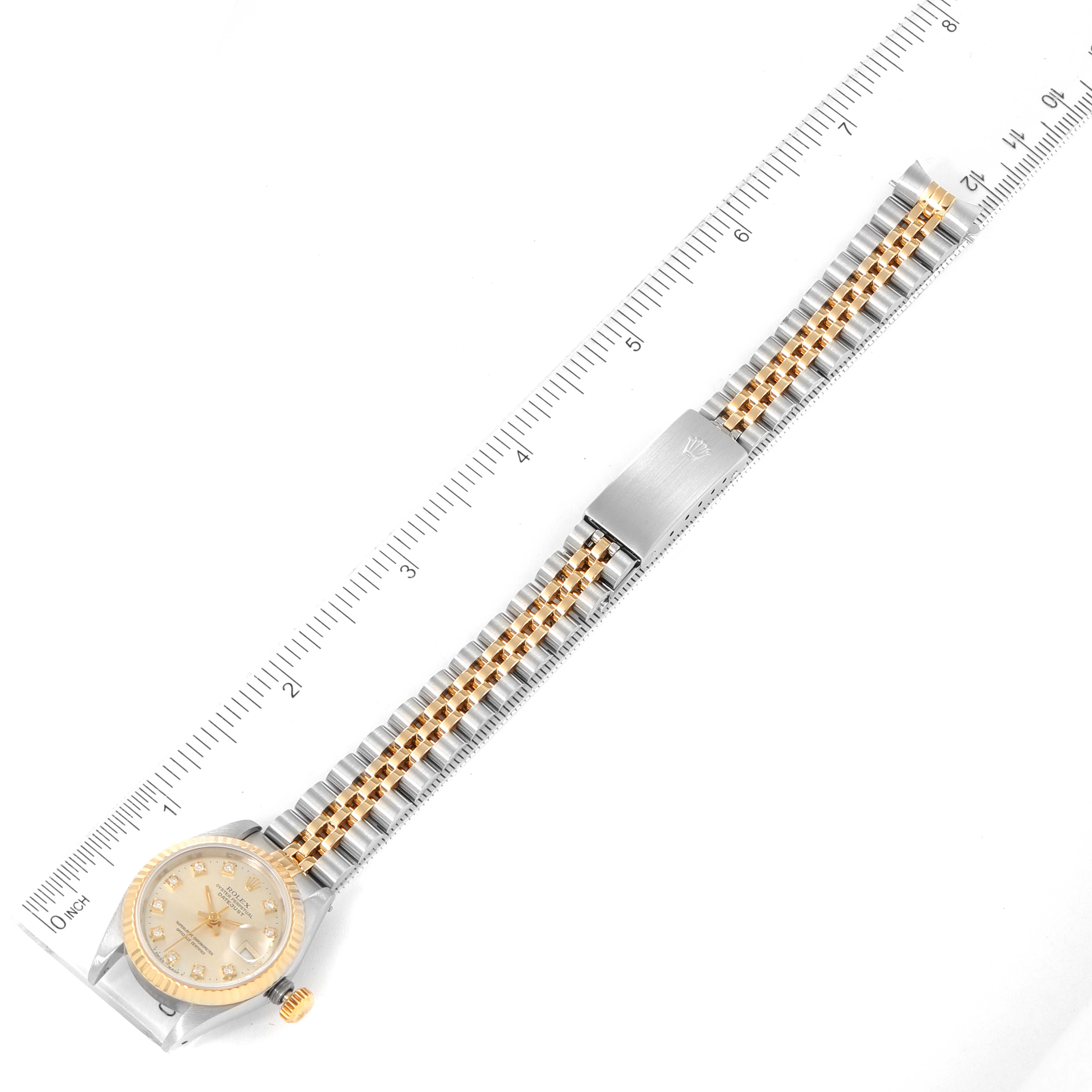 The image shows a Rolex Datejust 69173 Women
s Steel and Gold (two tone) Silver Dial 69173 Women
s Steel and Gold (two tone) Silver Dial watch laid flat, displaying its face, band, and clasp, with a ruler for size reference.