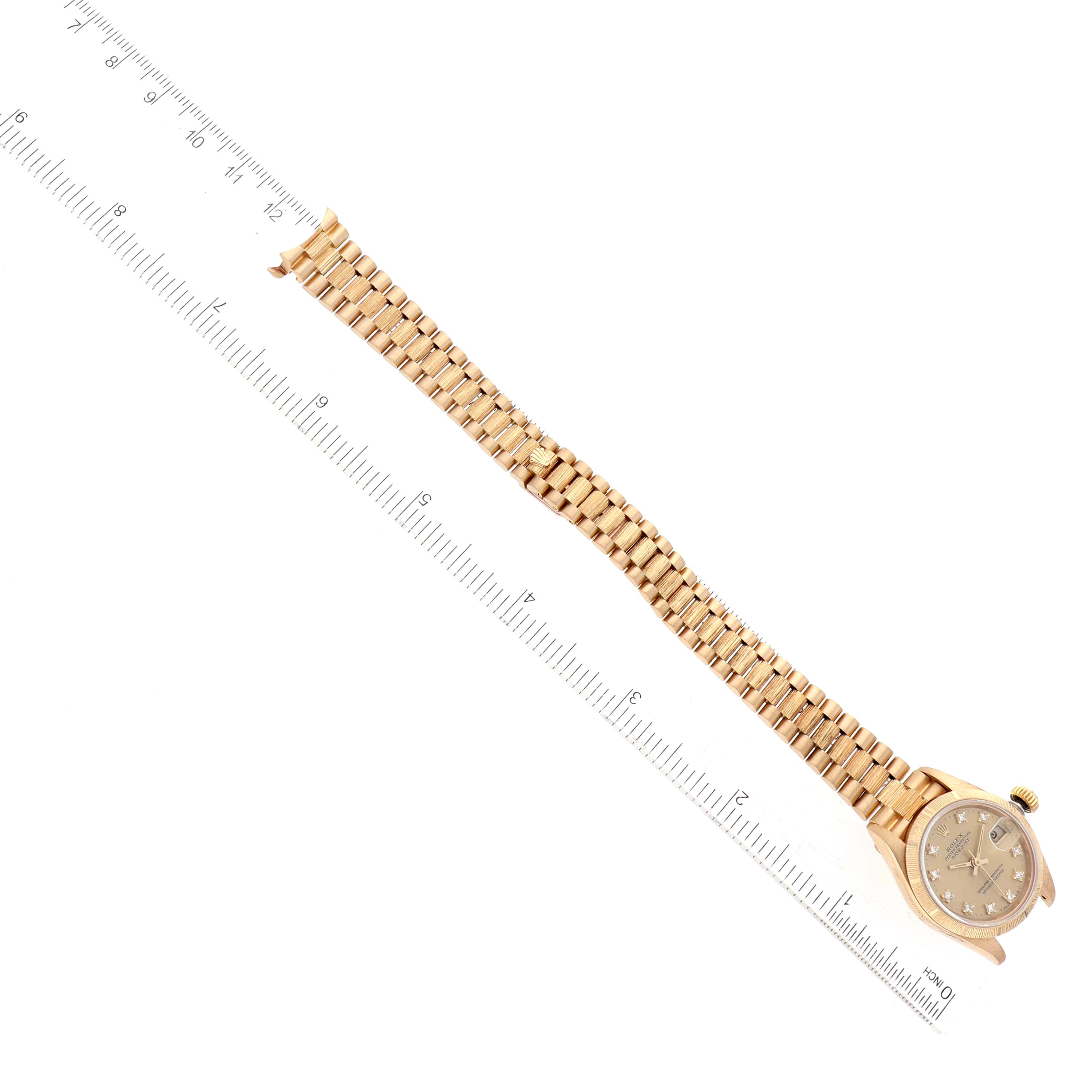 The image shows a Rolex President 69278G Women
s Yellow Gold Champagne Dial 69278G Women
s Yellow Gold Champagne Dial model watch from an overhead view, highlighting its face and full bracelet alongside a ruler.
