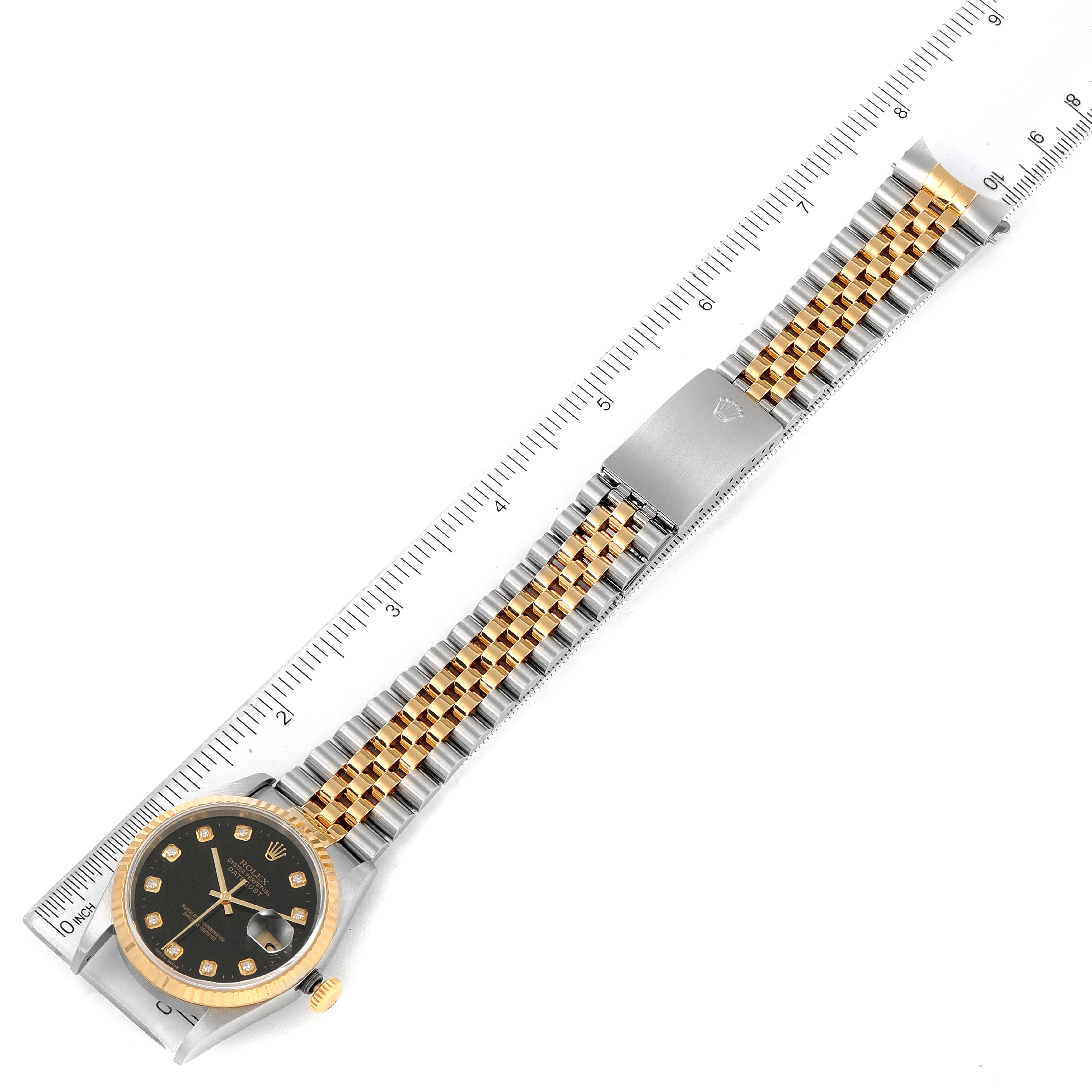 The image shows a Rolex Datejust 16233 Men's Steel and Gold (two tone) Black Dial 16233 Men's Steel and Gold (two tone) Black Dial watch laid flat, displaying the face, band, and clasp with a ruler for scale.