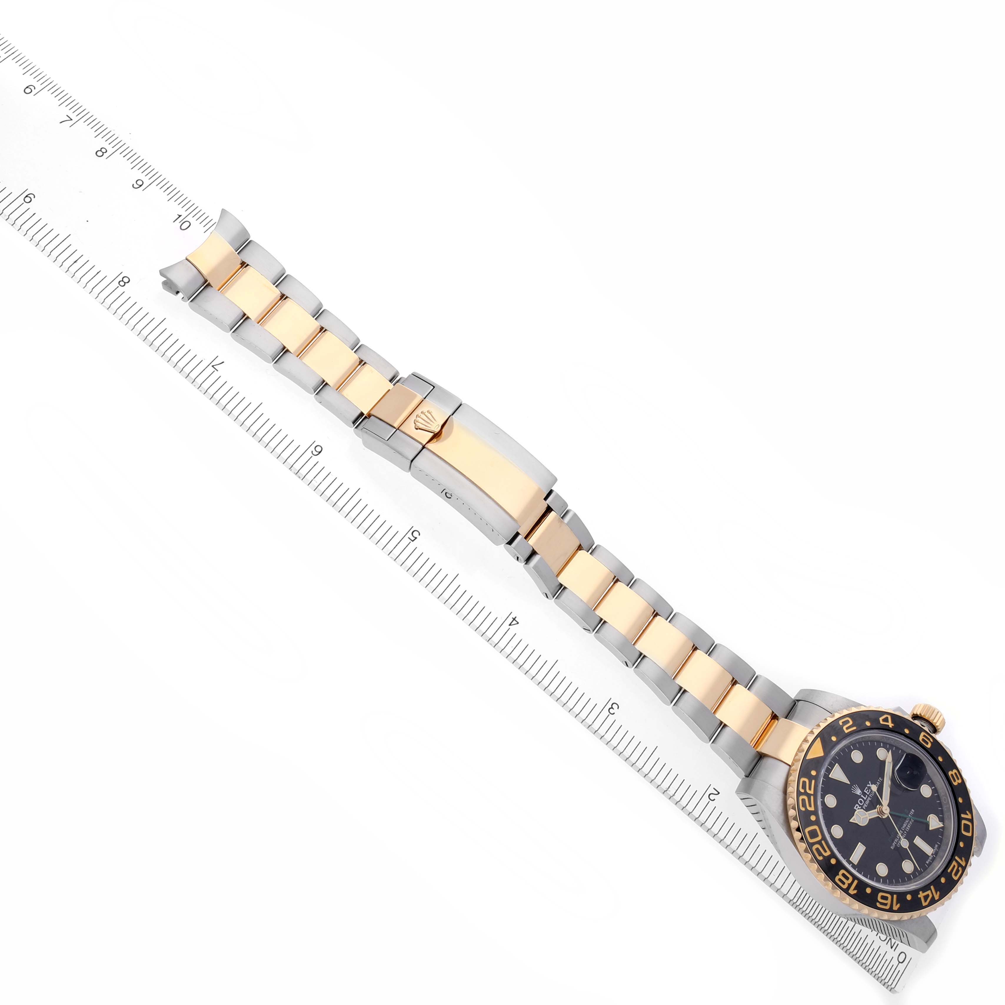 The Rolex GMT-Master 116713LN Men's Steel and Gold (two tone) Black Dial 116713LN Men's Steel and Gold (two tone) Black Dial watch is shown from an overhead angle, featuring the bracelet and clasp alongside a ruler.