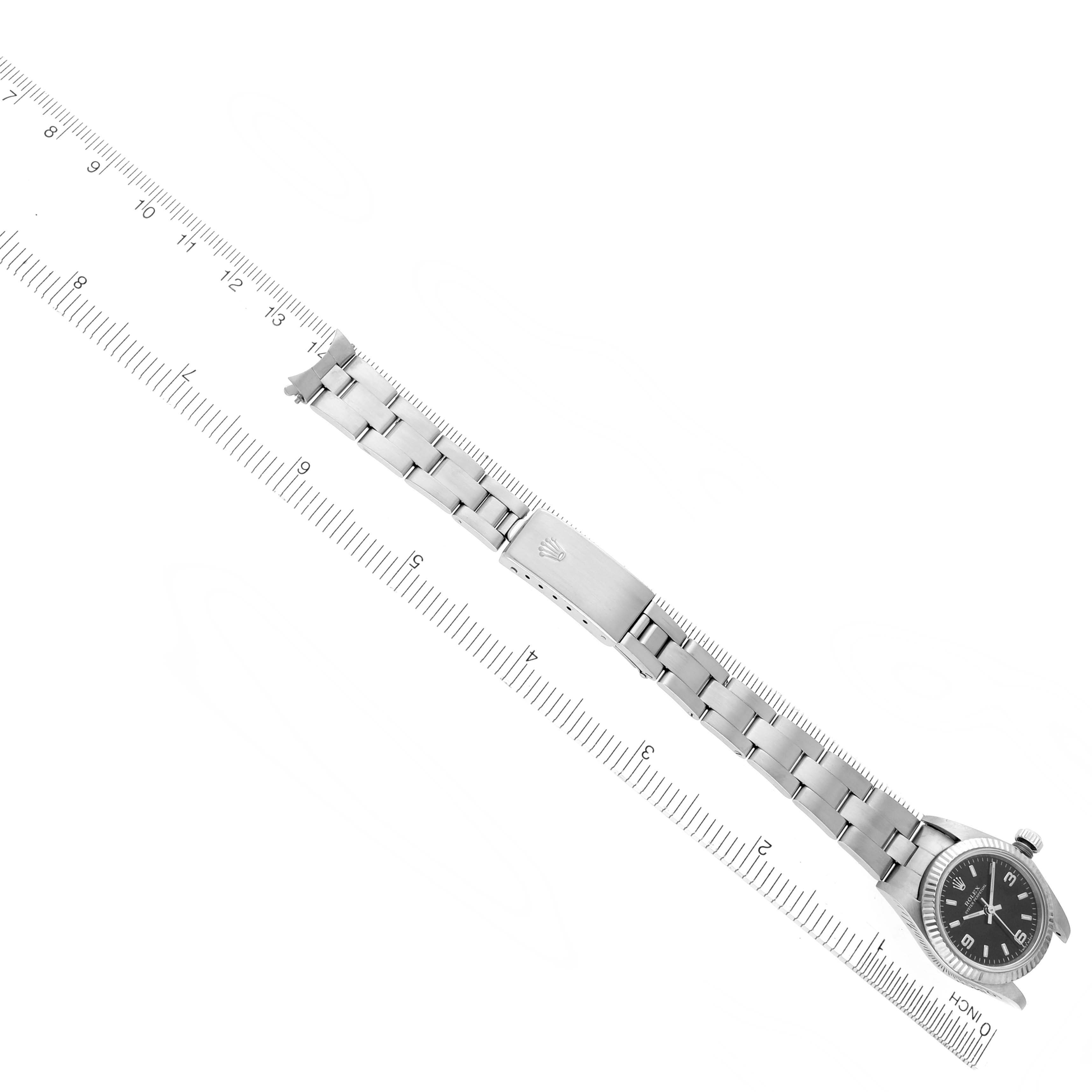 The image shows a Rolex Oyster Perpetual 76094 Women's Stainless Steel Black Dial 76094 Women's Stainless Steel Black Dial watch from a top perspective, highlighting its stainless steel bracelet and clasp along with a ruler for scale.