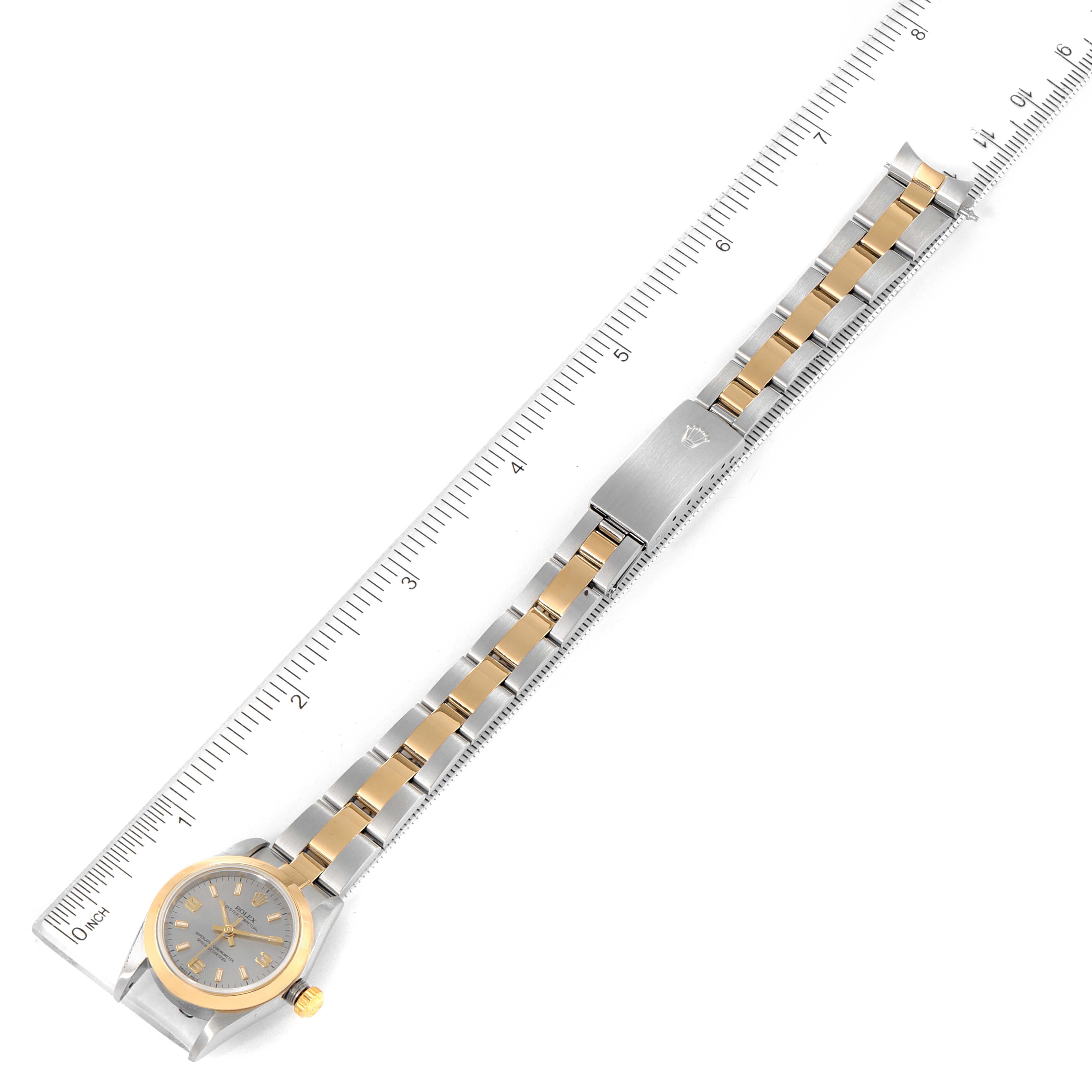 The image shows a full top-down view of a Rolex Oyster Perpetual 76183 Women's Steel and Gold (two tone) Grey Dial 76183 Women's Steel and Gold (two tone) Grey Dial watch, highlighting its face, bezel, bracelet, and clasp against a ruler.