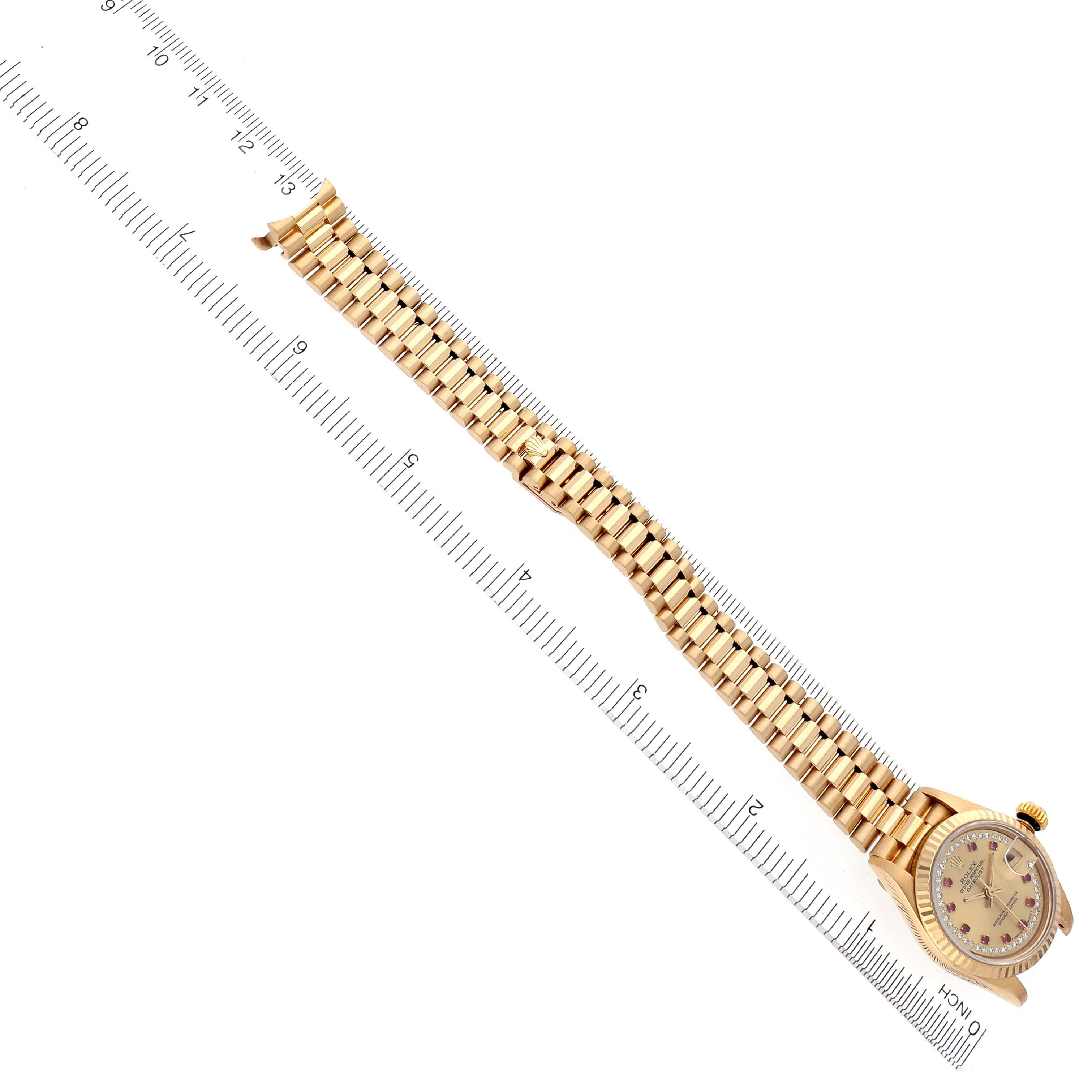 The image shows a Rolex President 69178 Women's Yellow Gold Champagne Dial 69178 Women's Yellow Gold Champagne Dial model watch laying flat with its bracelet extended beside a ruler.