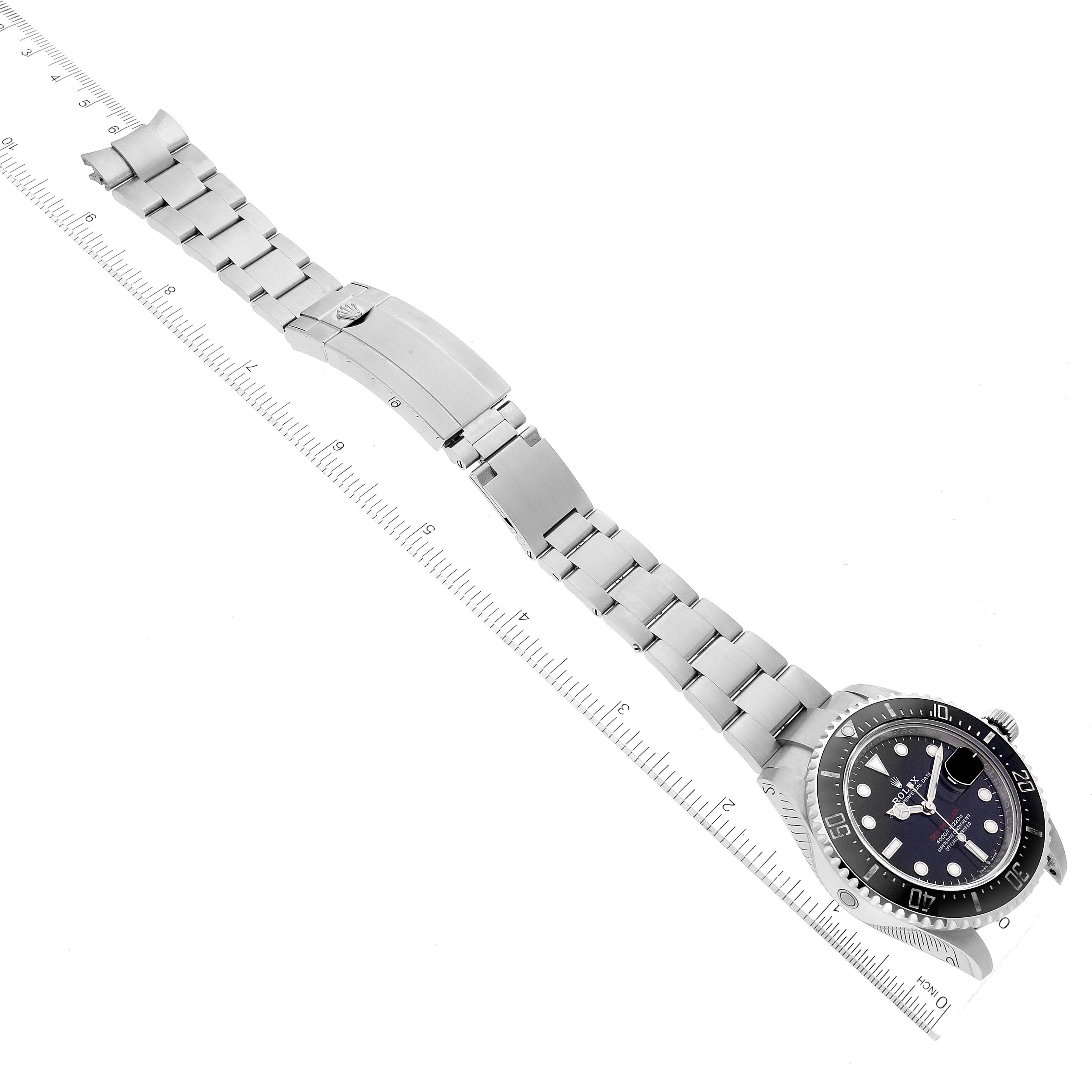 The image shows a Rolex Sea-Dweller 126600 Men
s Stainless Steel Black Dial 126600 Men
s Stainless Steel Black Dial watch laid flat with its full bracelet and dial facing upward, next to a ruler for scale.