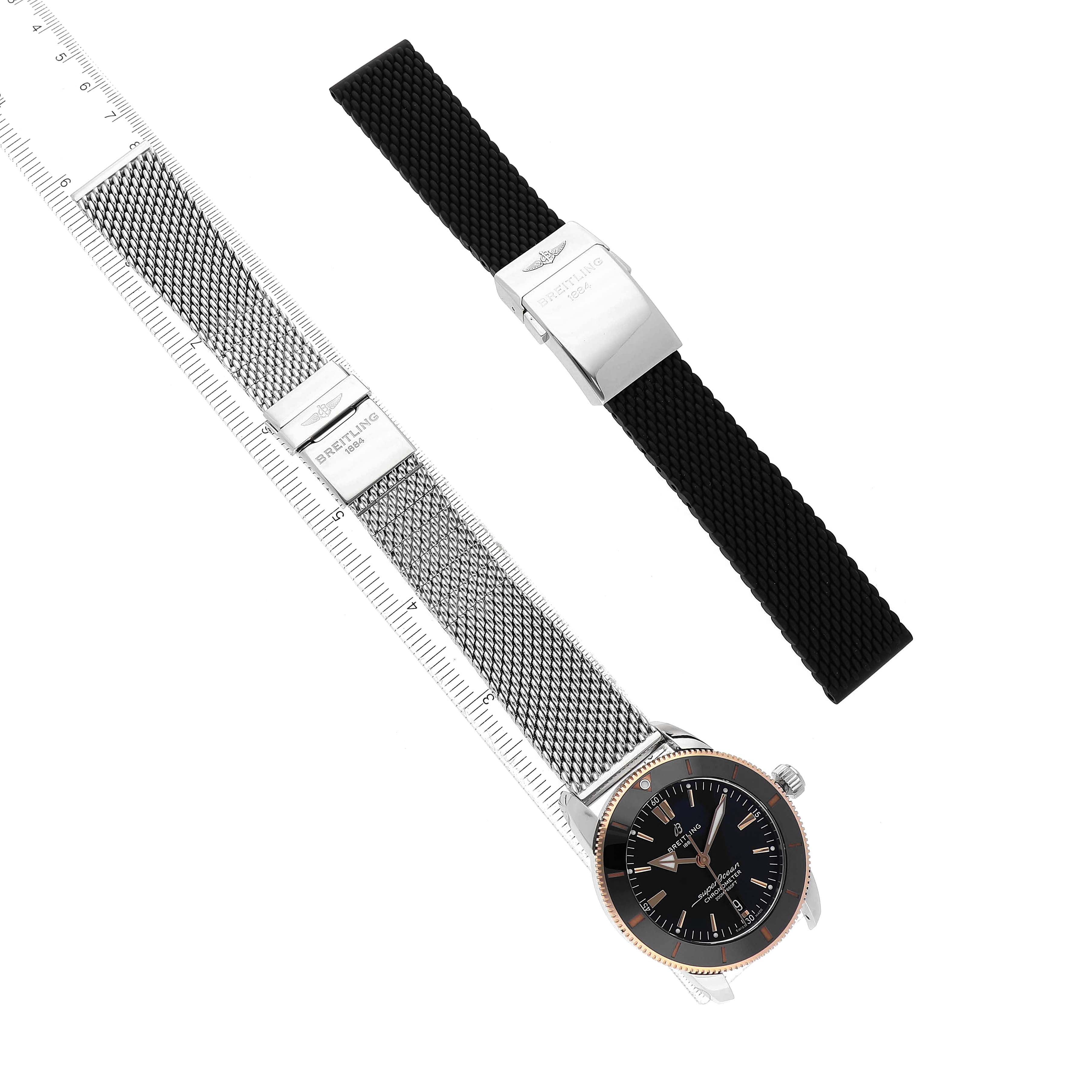 The Breitling Superocean UB2030 Men's Stainless Steel Black Dial is shown from a top-down angle, alongside a silver mesh bracelet and a black strap.