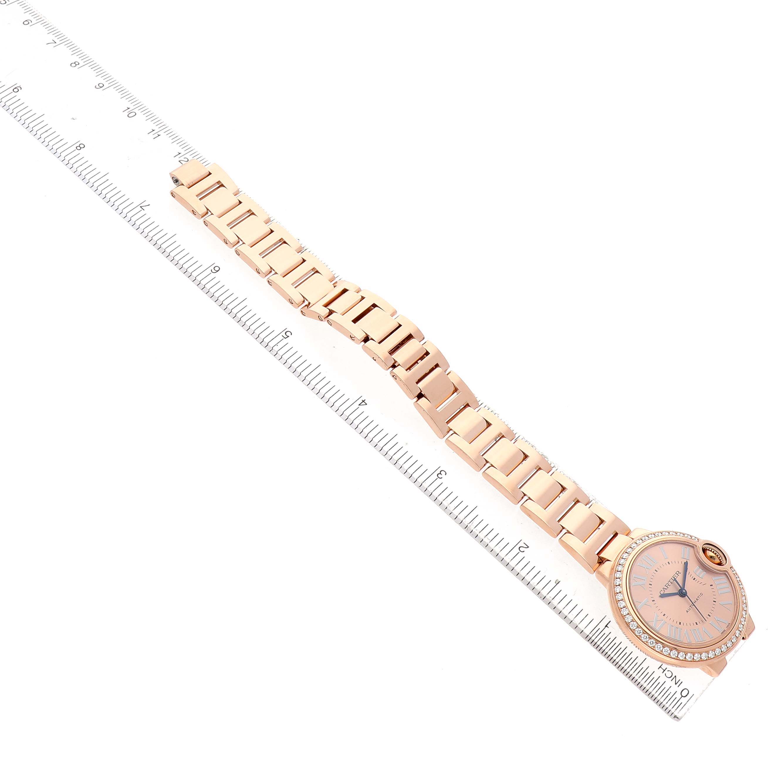 The image shows a top-down view of a Cartier Ballon Bleu WJBB0077 Women's Rose Gold Pink Dial watch with its bracelet laid straight beside a ruler.