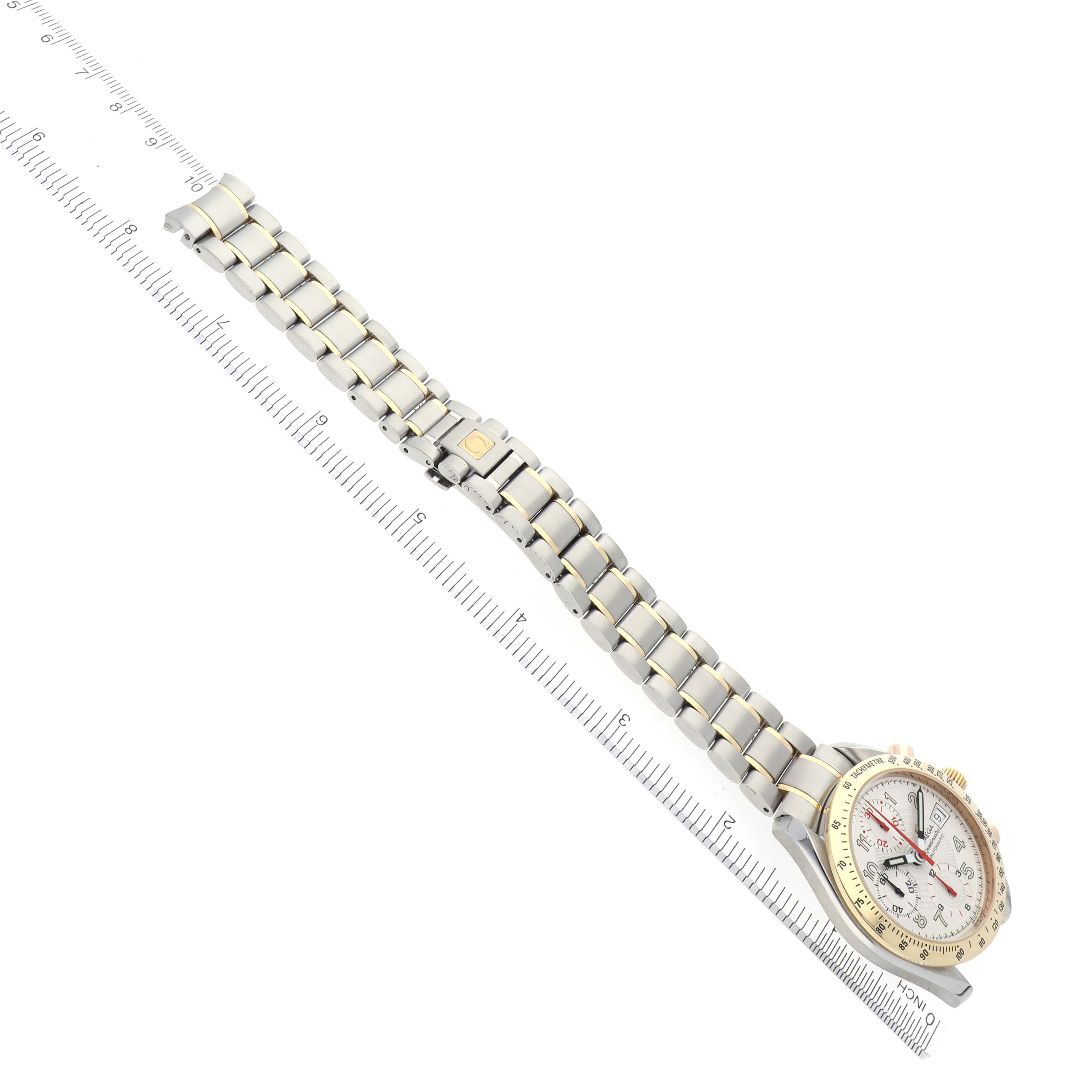 The Omega Speedmaster 3313.33.00 Men's Steel and Gold (two tone) White Dial 3313.33.00 Men's Steel and Gold (two tone) White Dial watch is shown at an angle highlighting its bracelet and clasp with a ruler for scale.