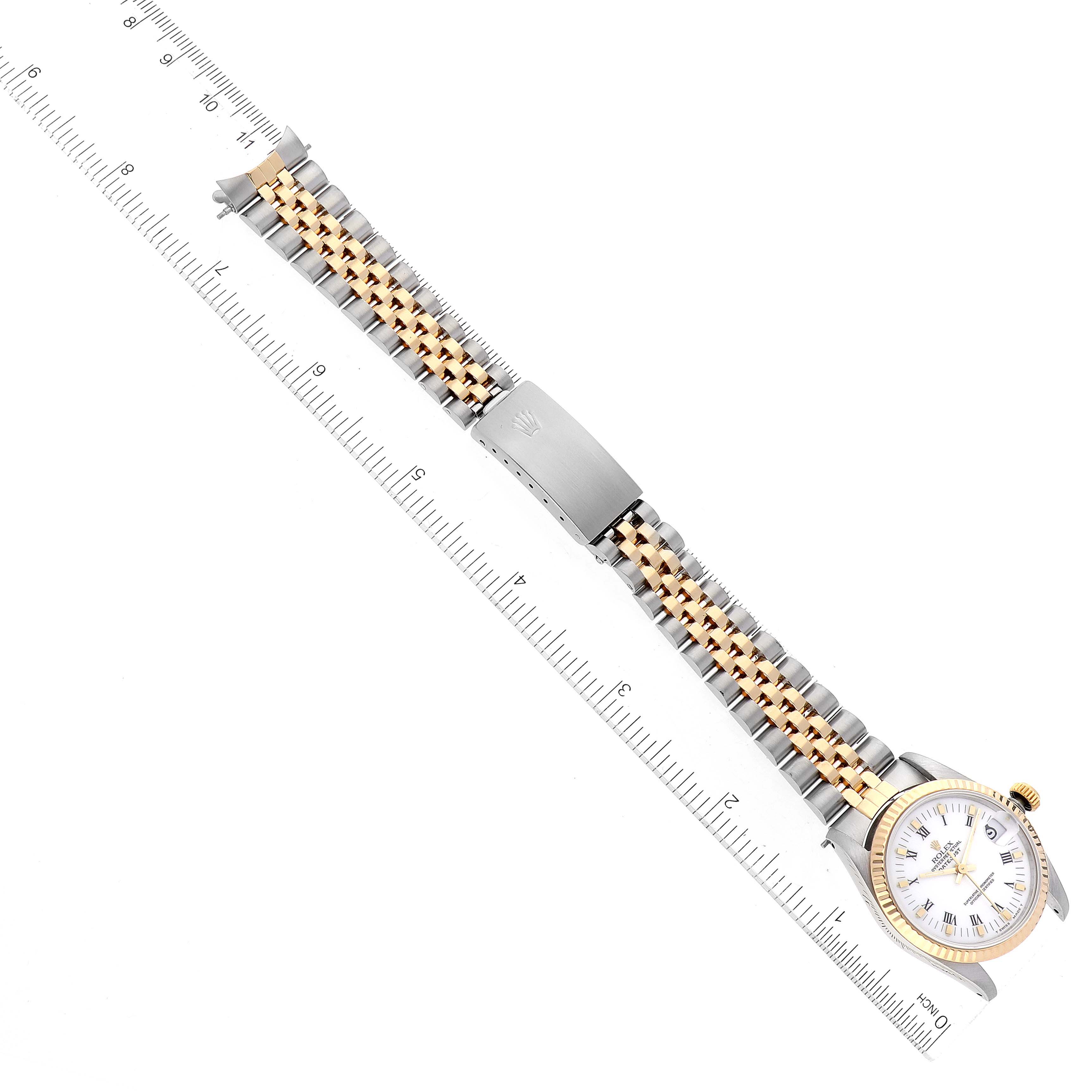 The image shows a top view of a Rolex Mid-Size 68273 Women
s Steel and Gold (two tone) White Dial 68273 Women
s Steel and Gold (two tone) White Dial watch with a two-tone metal band and a ruler for size reference.