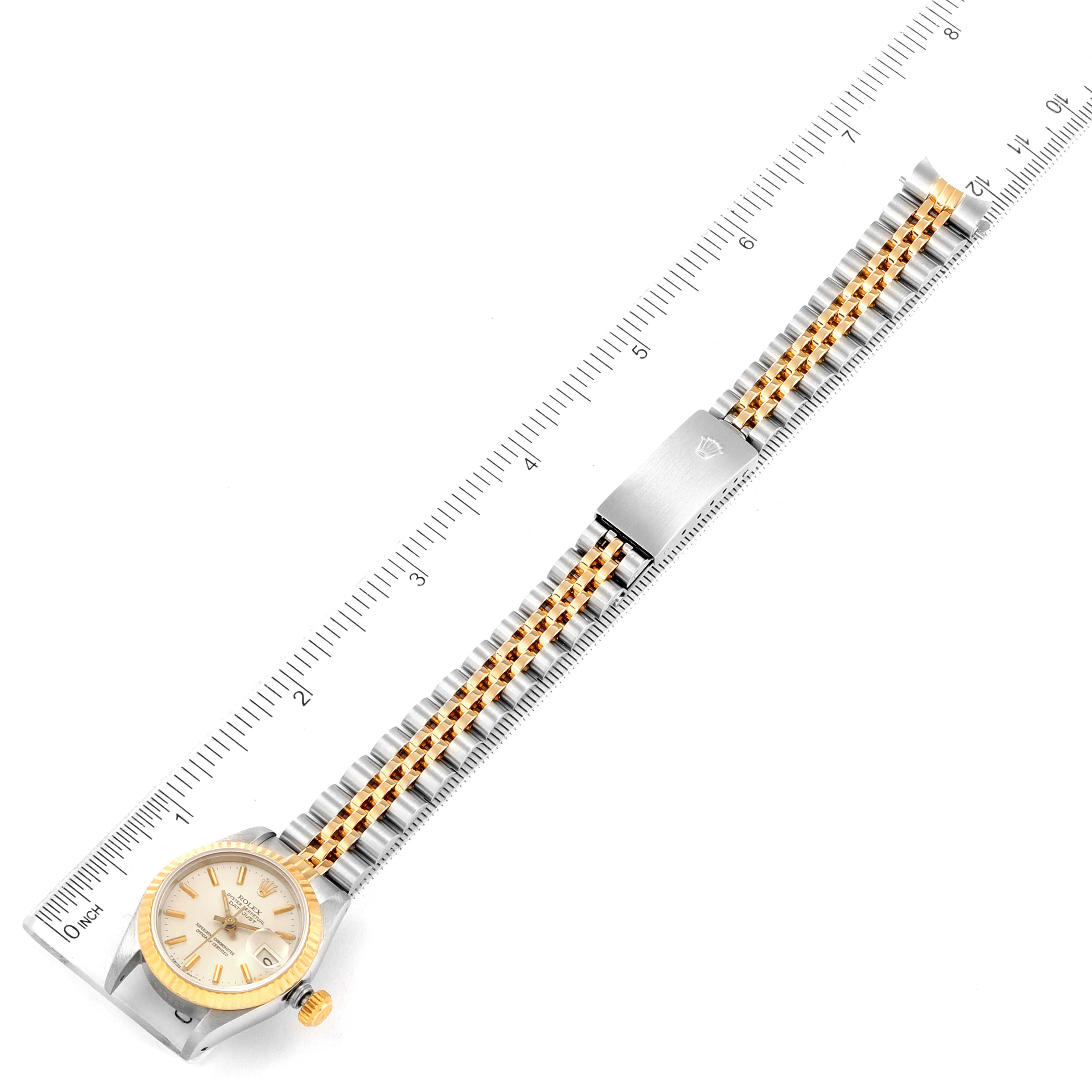 This image shows an overhead view of a Rolex Datejust 69173 Women
s Steel and Gold (two tone) Silver Dial 69173 Women
s Steel and Gold (two tone) Silver Dial watch with a dual-tone bracelet against a ruler for measurement.