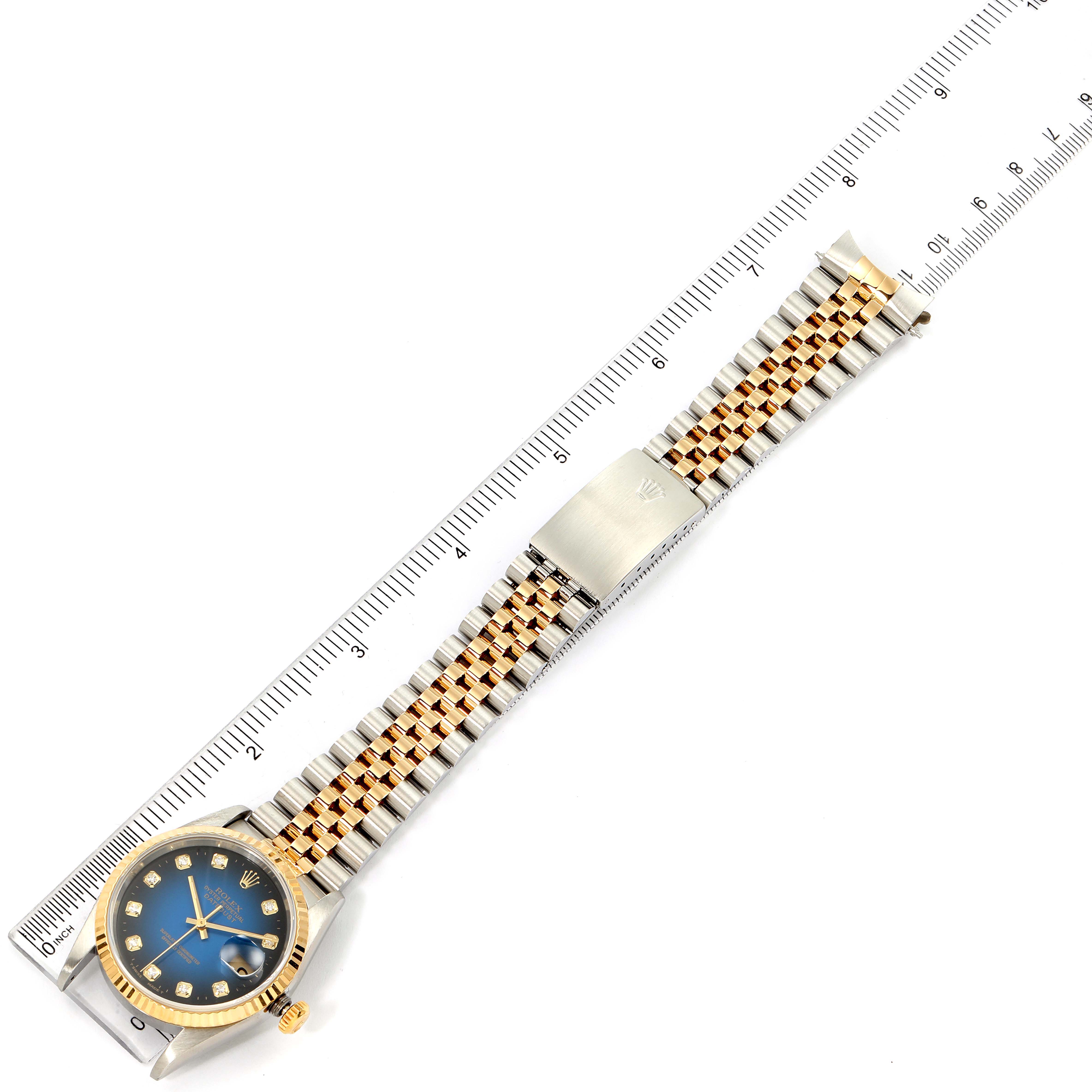 The Rolex Datejust 16233 Men's Steel and Gold (two tone) Blue Dial 16233 Men's Steel and Gold (two tone) Blue Dial watch is shown from a top-down angle, highlighting its face, bracelet, and clasp alongside a ruler.